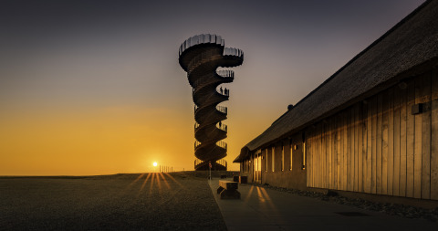 Marsk Camp glampingtent in Danimarca, torre a spirale al tramonto affiancata da un edificio in legno rustico.