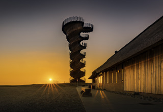 Marsk Camp glampingtenten in Denemarken, spiraalvormige toren bij zonsondergang en houten gebouw ernaast.