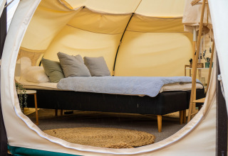 Intérieur d'une tente glamping au Marsk Camp au Danemark, avec lit douillet et ambiance chaleureuse.