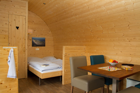 Vue intérieure d’un pod en bois confortable à Nordsee Camp-Norddeich avec lit, table à manger et chaises.