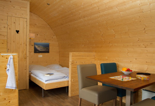 Vista interna di un'accogliente pod in legno al Nordsee Camp-Norddeich con letto, tavolo e sedie.