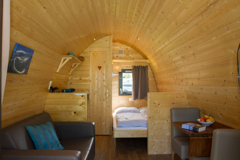 Interior of a glamping pod at Nordsee Camp-Norddeich with wood walls, sofa, dining table, and bed.