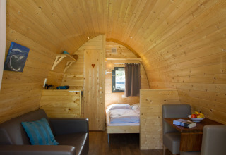 Innenansicht eines Glamping-Pods mit Holzverkleidung, Sofa, Bett und Tisch, Nordsee Camp-Norddeich.