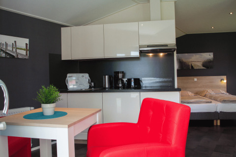 Modernes Glamping-Apartment mit Küchenzeile, Doppelbett, rotem Sessel und stilvollem Interieur im Nordsee Camp-Norddeich.