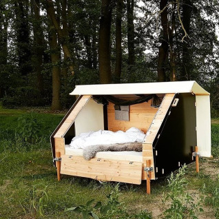 Alojamiento glamping WERKHAUS destinature en un bosque, con cama cómoda y estructura de madera.