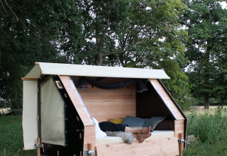A person relaxes in a modern wooden glamping pod situated outdoors, surrounded by lush greenery and trees.