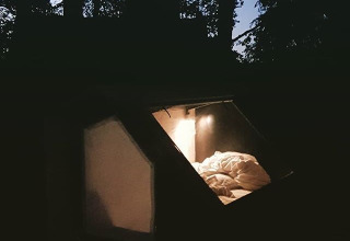 Glampingaccommodatie WERKHAUS destinature - Glamping Nedersaksen, gezellige verlichte tent in bos bij avond.