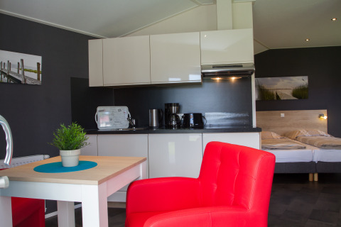 Alojamiento glamping moderno en Nordsee Camp-Norddeich, con cocina, cama y silla roja en Oost-Friesland.