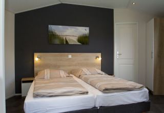 Moderne chalet-soveværelse med to enkeltsenge, mørk accentvæg og naturbillede på Nordsee Camp