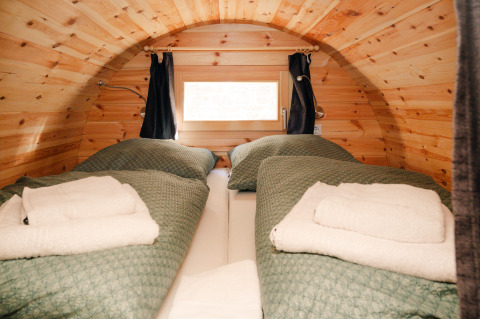 Cozy glamping accommodation inside a rustic wine barrel with twin beds and green covers on the German Wine Route.