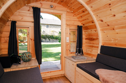 Interno di una botte in legno per glamping, con tende scure e vista sul giardino a Bockenheim, Pfalz.