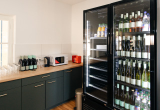 Coin cuisine d’un hébergement glamping avec bouteilles de vin, verres, micro-ondes et frigo garni de boissons.