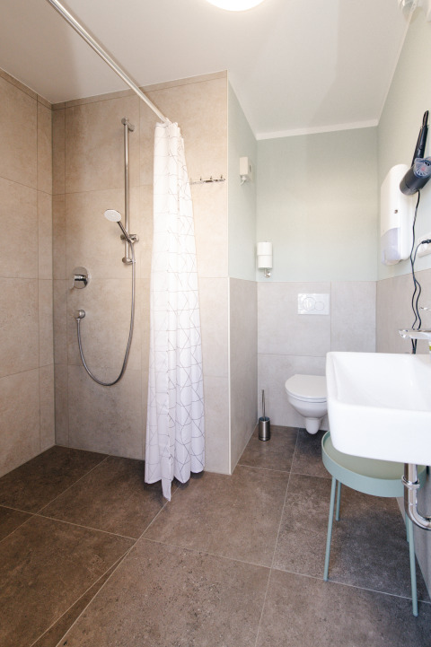 Modern bathroom with shower, curtain, sink, and toilet in glamping wine barrel accommodation in Bockenheim, Pfalz.