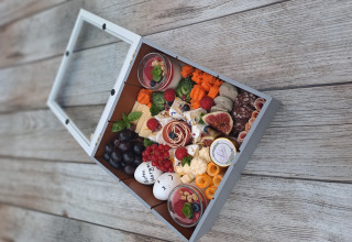 Luksus picnic-boks med ost, kød, frugt og desserter på træbord ved Rustieke wijnvaten Glamping Bockenheim.