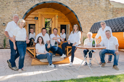 Familie vor rustikalen Weinfass-Unterkünften bei Glamping Weinroute Bockenheim, Pfalz, genießt die Sonne.