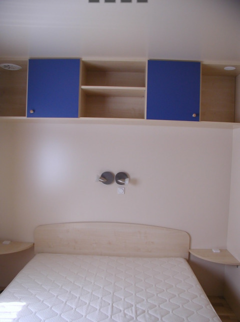 Interno di una camera glamping al Camping Rosental Roz con letto, scaffali e armadietti blu sopra.