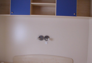 Interieur van een glampingkamer bij Camping Rosental Roz met bed, planken en blauwe kastjes erboven.