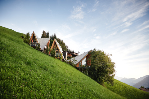 Alloggio glamping HochLeger Chalet Refugium - Boomhut Tirol situato su un pendio erboso e ripido tra le montagne.