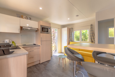 Moderne Glamping-Unterkunft bei Camping Bonporteau mit Küche, gelber Sitzecke und Fensterblick in Südfrankreich.