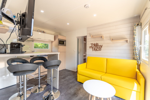 Helles Glamping-Wohnzimmer in Camping Bonporteau, Südfrankreich, mit gelbem Sofa und moderner Küche.