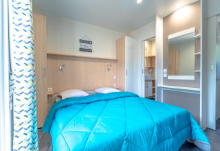 Alloggio glamping al Camping Bonporteau con letto matrimoniale, armadio e specchio grande.