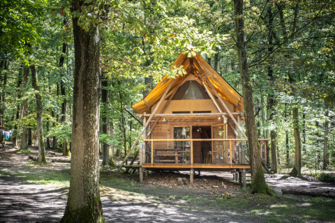 Glamping-Unterkunft im Wald bei Huttopia Versailles - Glamping Île de France, rustikale Holzhütte in grüner Umgebung.