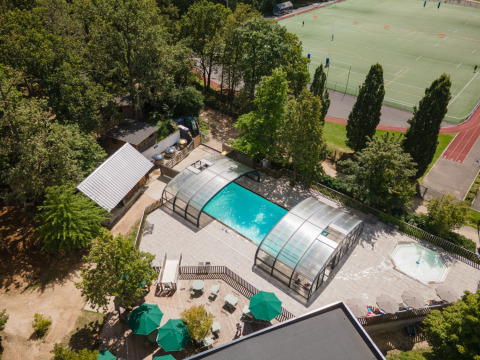 Piscine extérieure couverte et terrain de sport à proximité à Huttopia Versailles - Glamping Île de France, entouré d’arbres.
