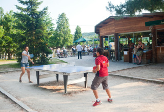Due persone giocano a ping pong all’aperto vicino a una baita a Huttopia Versailles - Glamping Île de France.