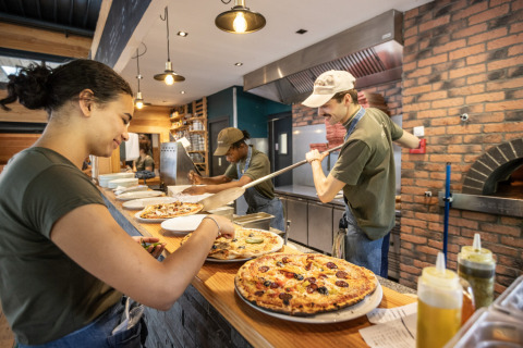 Mitarbeiter bereiten frische Pizza in einer gemütlichen Küche im Huttopia Versailles - Glamping Île de France zu.