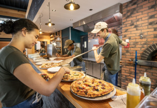 Mitarbeiter bereiten frische Pizza in einer gemütlichen Küche im Huttopia Versailles - Glamping Île de France zu.