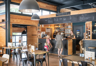 Cafetería moderna con interior de madera en Huttopia Versailles - Glamping Île de France, clientes en la barra.