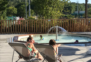 Kinder entspannen auf Liegestühlen neben einem flachen Pool mit Springbrunnen bei Huttopia Versailles Glamping.