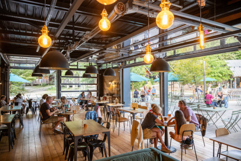 Salle à manger intérieure chaleureuse avec grandes baies vitrées et vue sur la terrasse chez Huttopia Versailles.