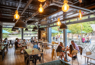 Salle à manger intérieure chaleureuse avec grandes baies vitrées et vue sur la terrasse chez Huttopia Versailles.