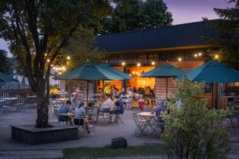 Terraza al aire libre de Huttopia Versailles - Glamping Île de France con invitados, luces y sombrillas verdes al atardecer.