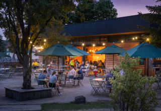 Terraza al aire libre de Huttopia Versailles - Glamping Île de France con invitados, luces y sombrillas verdes al atardecer.