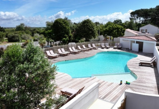 Buitenzwembad met houten dek, ligstoelen en veel groen bij Le Bellevue – Cottages en lodges Vendée.