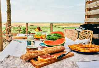 Ontbijttafel buiten met fruit, watermeloen, brood en croissants bij Le Bellevue – Cottages en lodges Vendée.