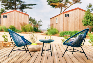 Buitenterras met blauwe stoelen en houten huisjes bij Le Bellevue – Cottages en lodges Vendée, ontspannen sfeer.