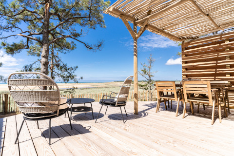 Zonnig terras bij Le Bellevue – Cottages en lodges Vendée met houten stoelen en uitzicht op strand en duinen.