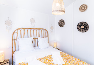 Lichte, gezellige slaapkamer in 'Le Bellevue – Cottages en lodges Vendée' met rotan hoofdboard en wanddecoraties.