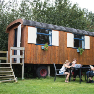 Familie nyder tid udenfor en træ-pipowagen ved Familiecamping Hendriks Wijkje i Drenthe, Holland.