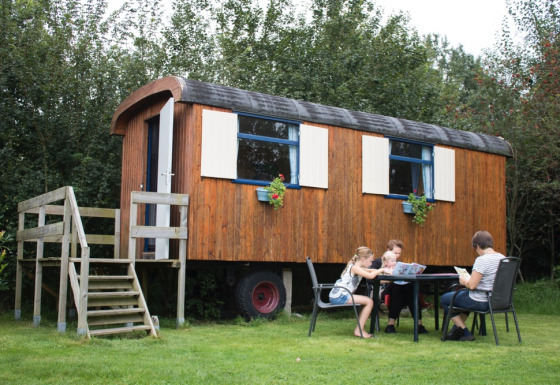 Gezin zit buiten bij een houten pipowagen op Familiecamping Hendriks Wijkje in Drenthe, Nederland.