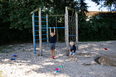 To børn leger på en legeplads med klatrestativ og sand ved Familiecamping Hendriks Wijkje - Pipowagens Drenthe.