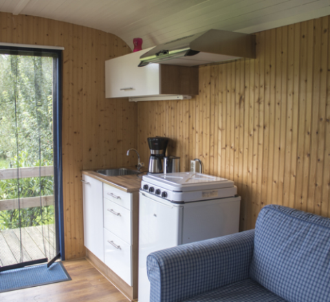 Vista interior de un alojamiento glamping con cocina, sofá y paredes de madera en Familiecamping Hendriks Wijkje - Pipowagens Drenthe.