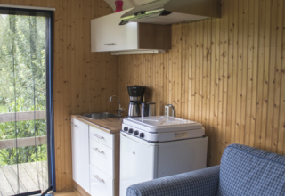 Vue intérieure d’un hébergement glamping avec kitchenette, canapé et murs en bois à Familiecamping Hendriks Wijkje - Pipowagens Drenthe.