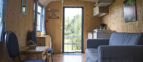 Interior of a cozy glamping pipowagen at Familiecamping Hendriks Wijkje in Drenthe, featuring sofa and kitchen.