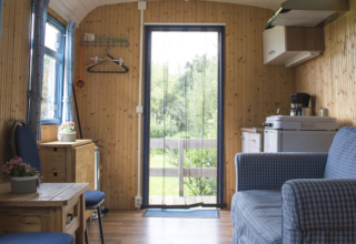 Indretning af en hyggelig pipowagen på Familiecamping Hendriks Wijkje i Drenthe med sofa og tekøkken.