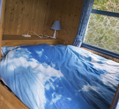 Slaapkamer in glampingaccommodatie bij Familiecamping Hendriks Wijkje, met een dekbedovertrek met luchtmotief.