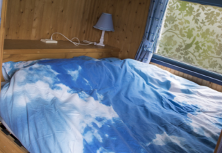 Slaapkamer in glampingaccommodatie bij Familiecamping Hendriks Wijkje, met een dekbedovertrek met luchtmotief.